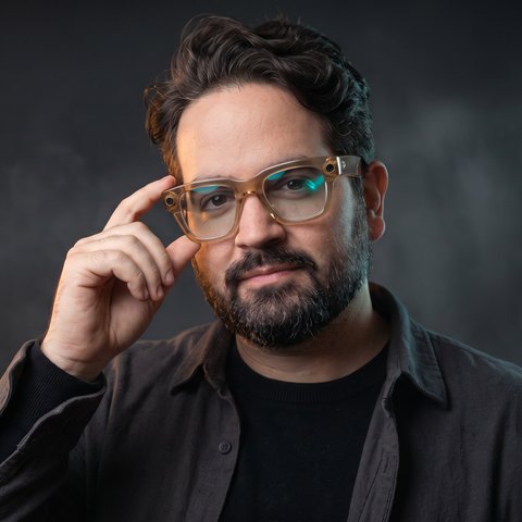 Leo Blume, dark shirt, adjusting his glasses and looking at the camera.